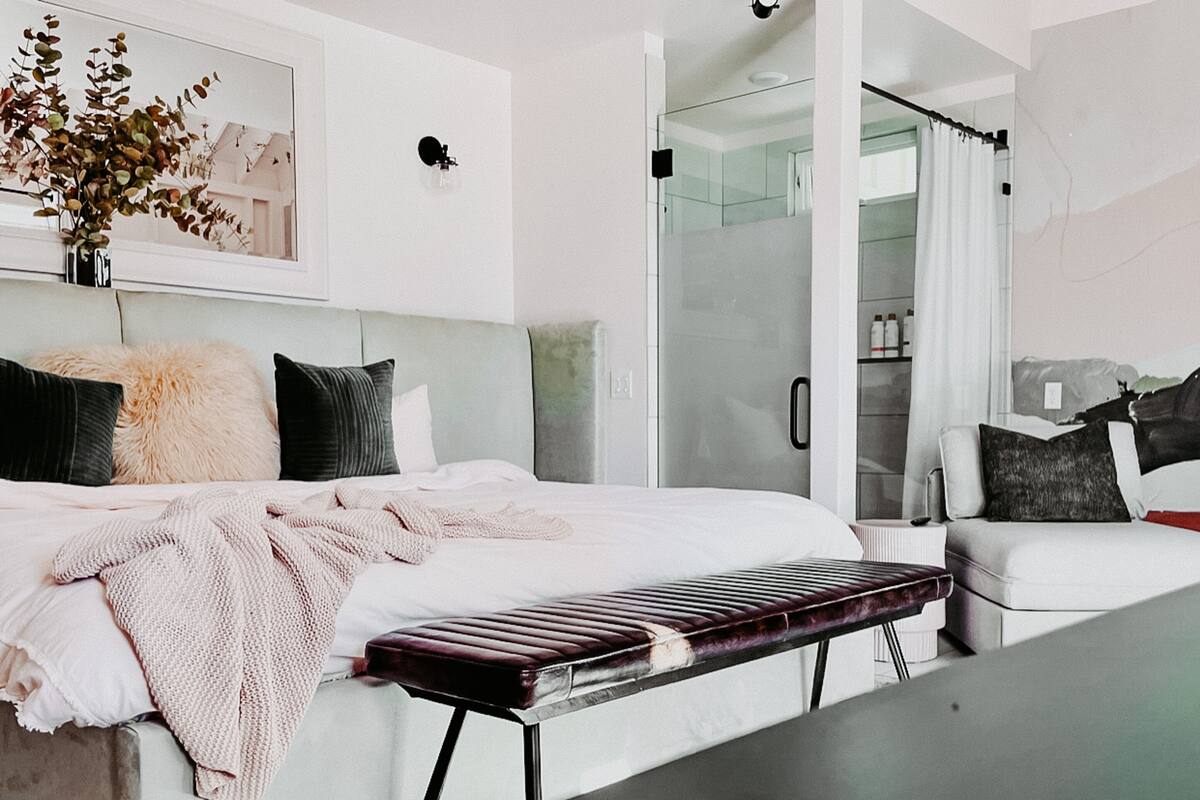 A modern bedroom with a bed, bench, and a glass shower area.