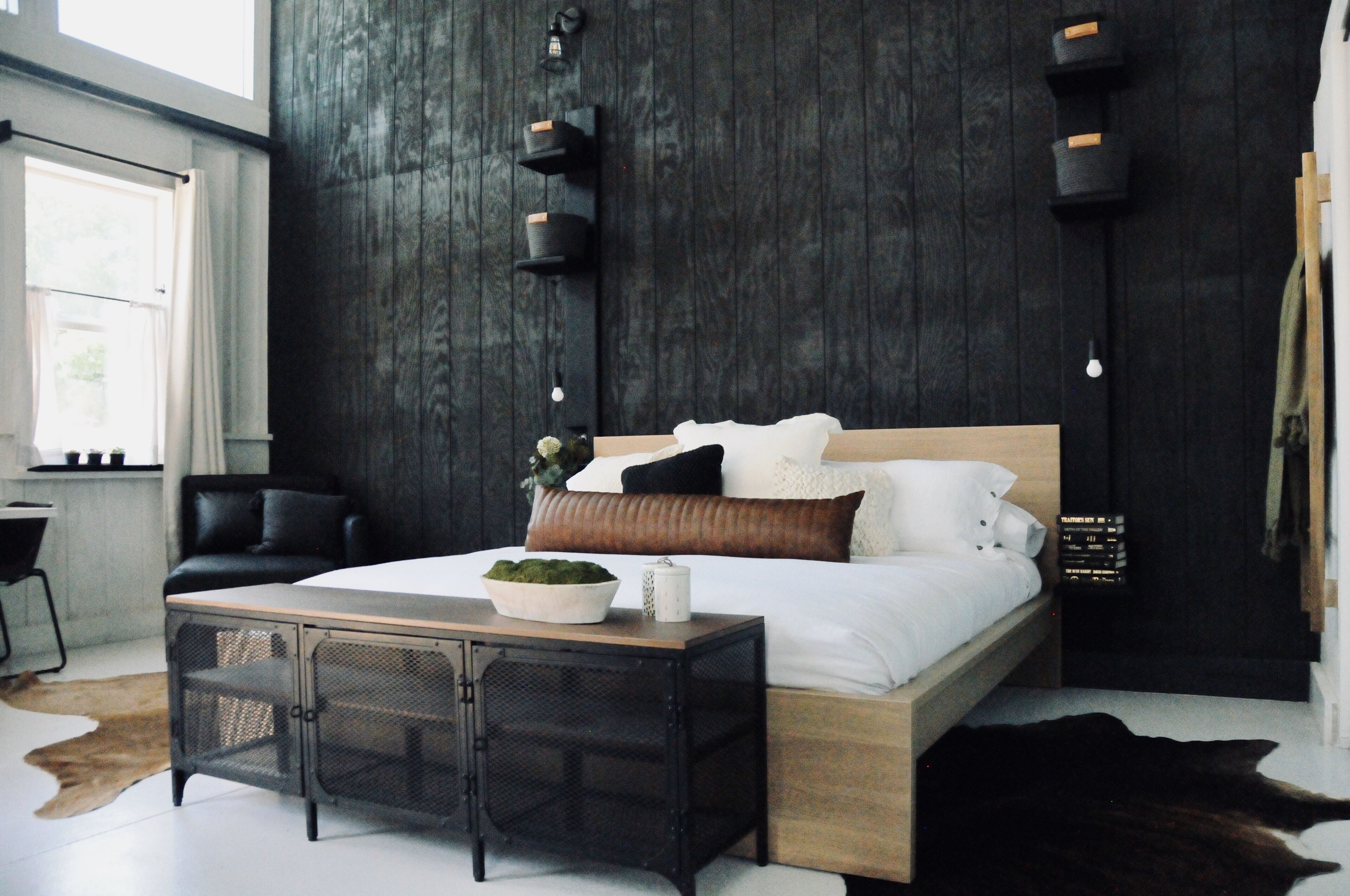 Ein modernes Schlafzimmer mit einem hölzernen Bett, schwarz-weißer Bettwäsche, einem kleinen Nachttisch und einem schwarzen Ledersessel.
