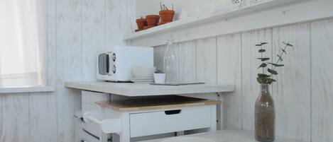 Uma cozinha com armários brancos, micro-ondas, cafeteira e um vaso com planta.