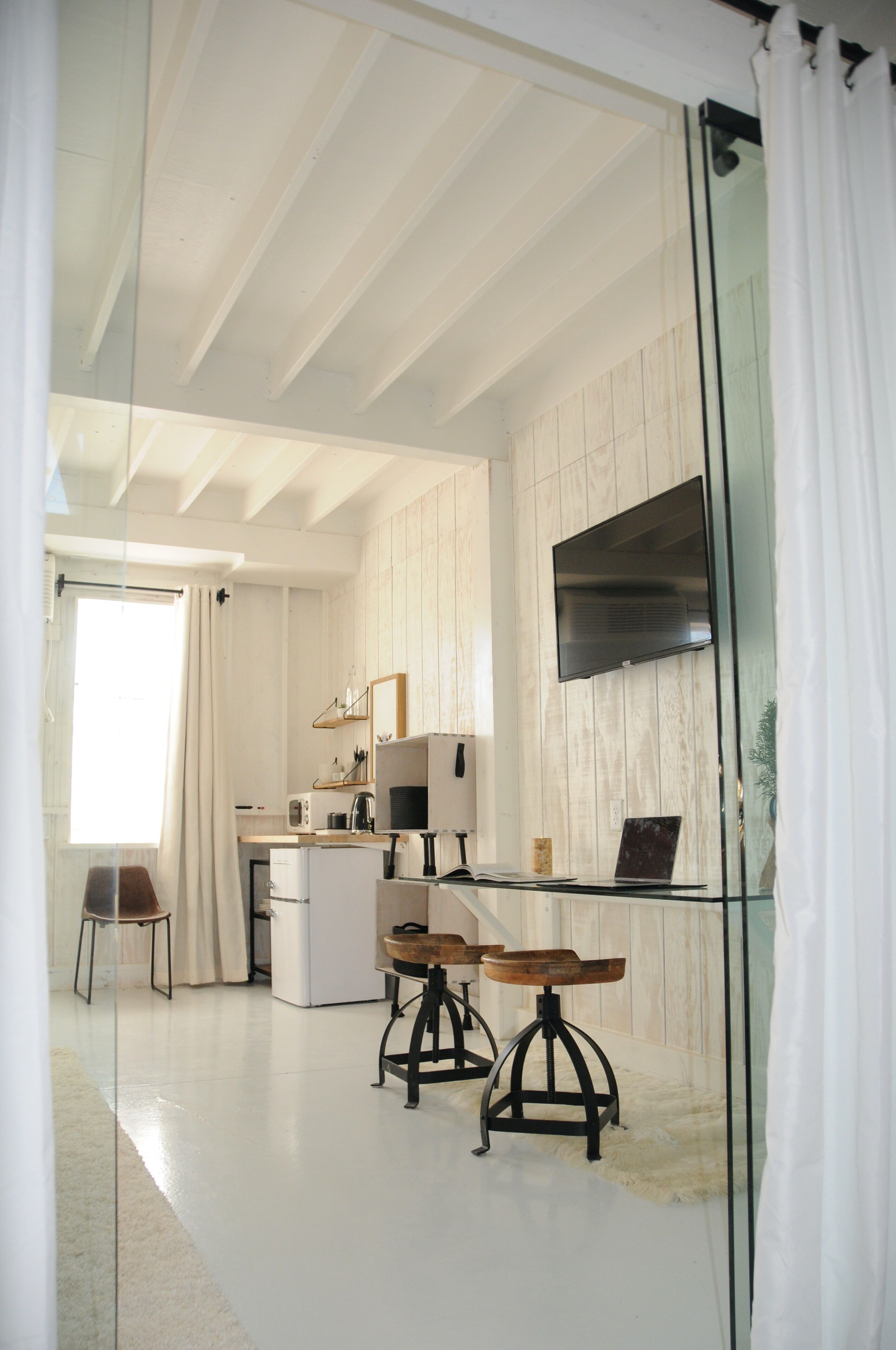 A modern kitchen with a large window, white cabinetry, a flat-screen TV, and a dining area with stools.