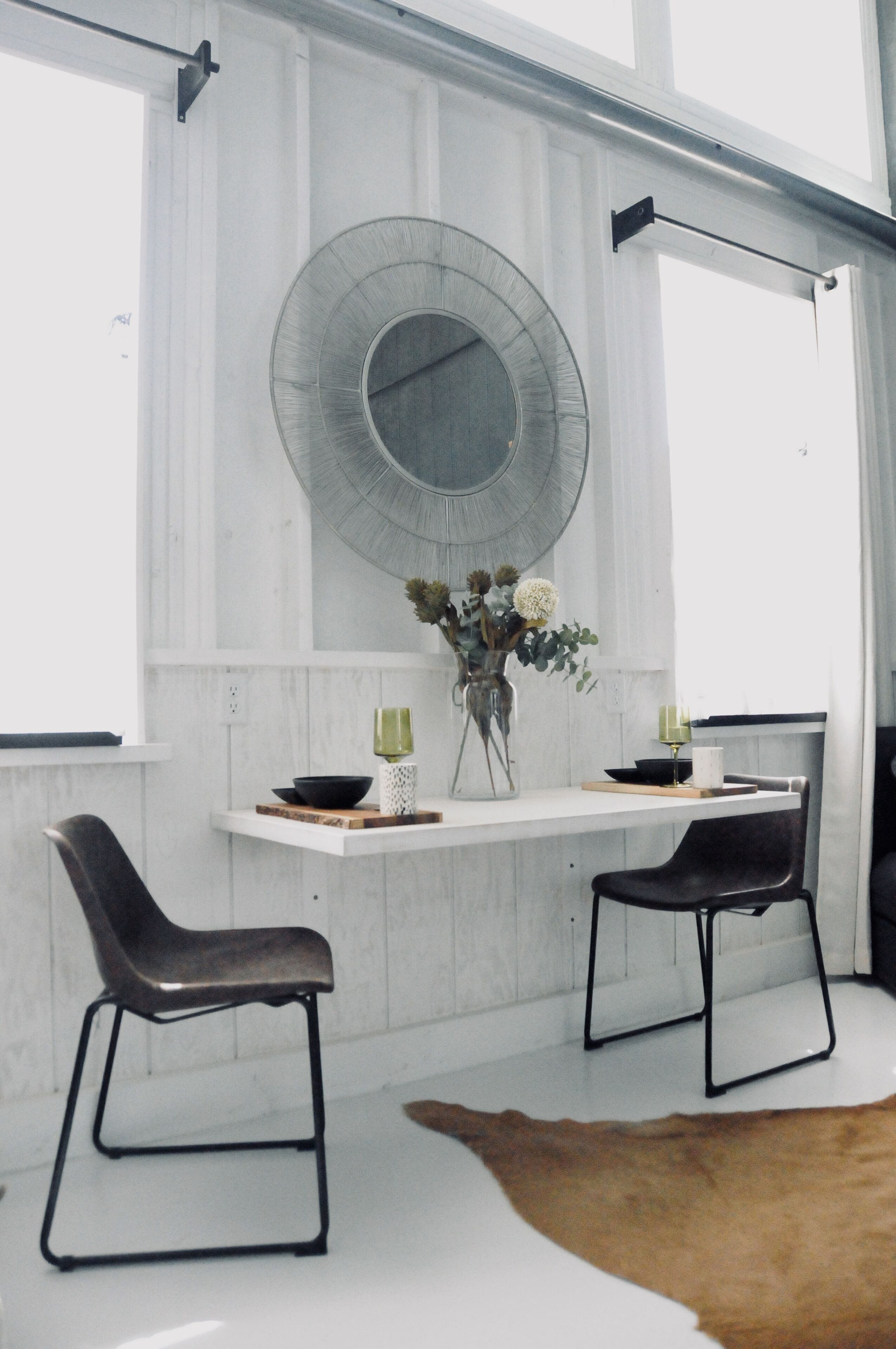 Un comedor con una mesa blanca, dos sillas negras, una obra de arte de vidrio y una alfombra marrón.
