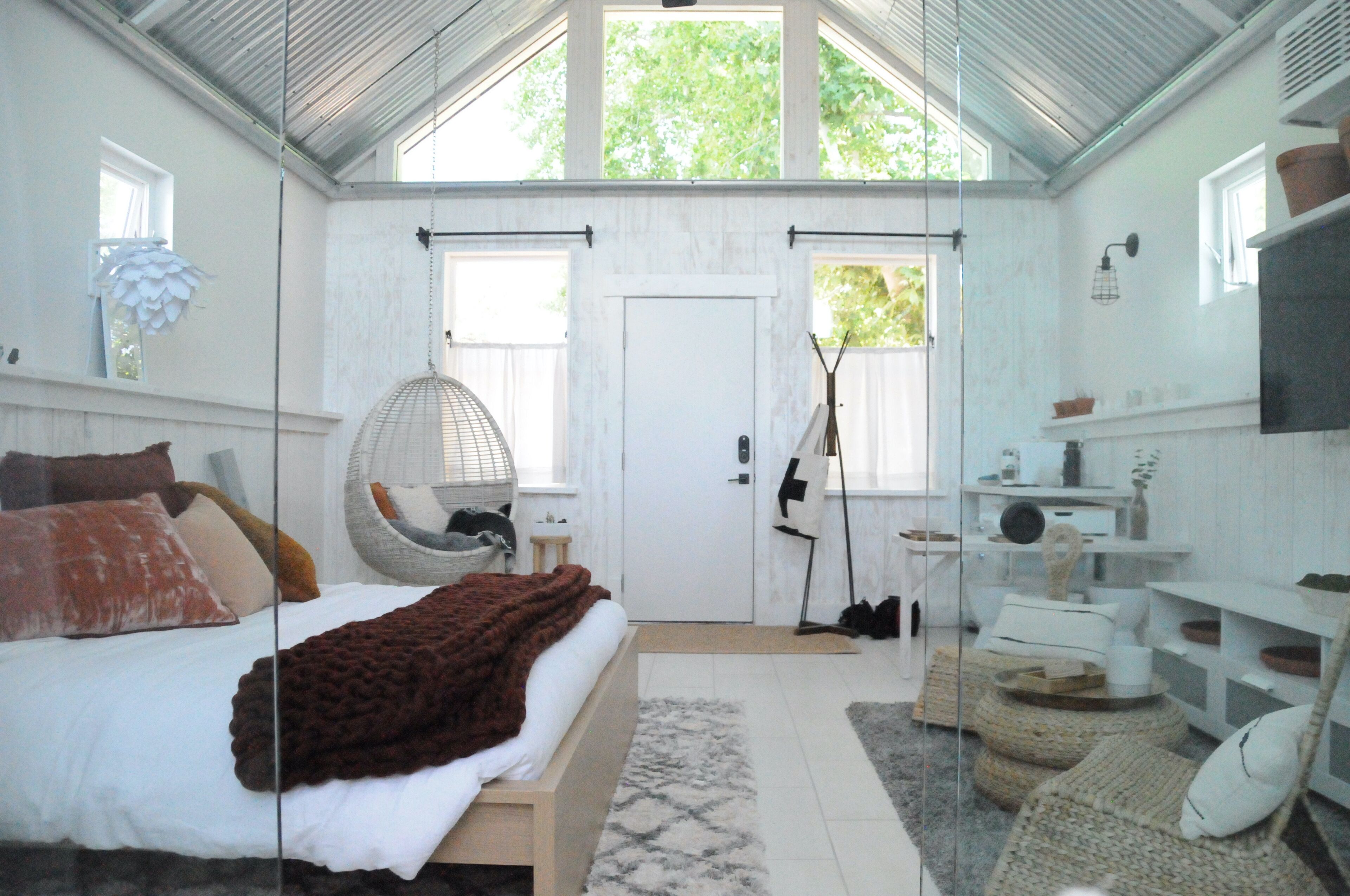 A bedroom with a bed, a hanging chair, a wardrobe, and a TV.