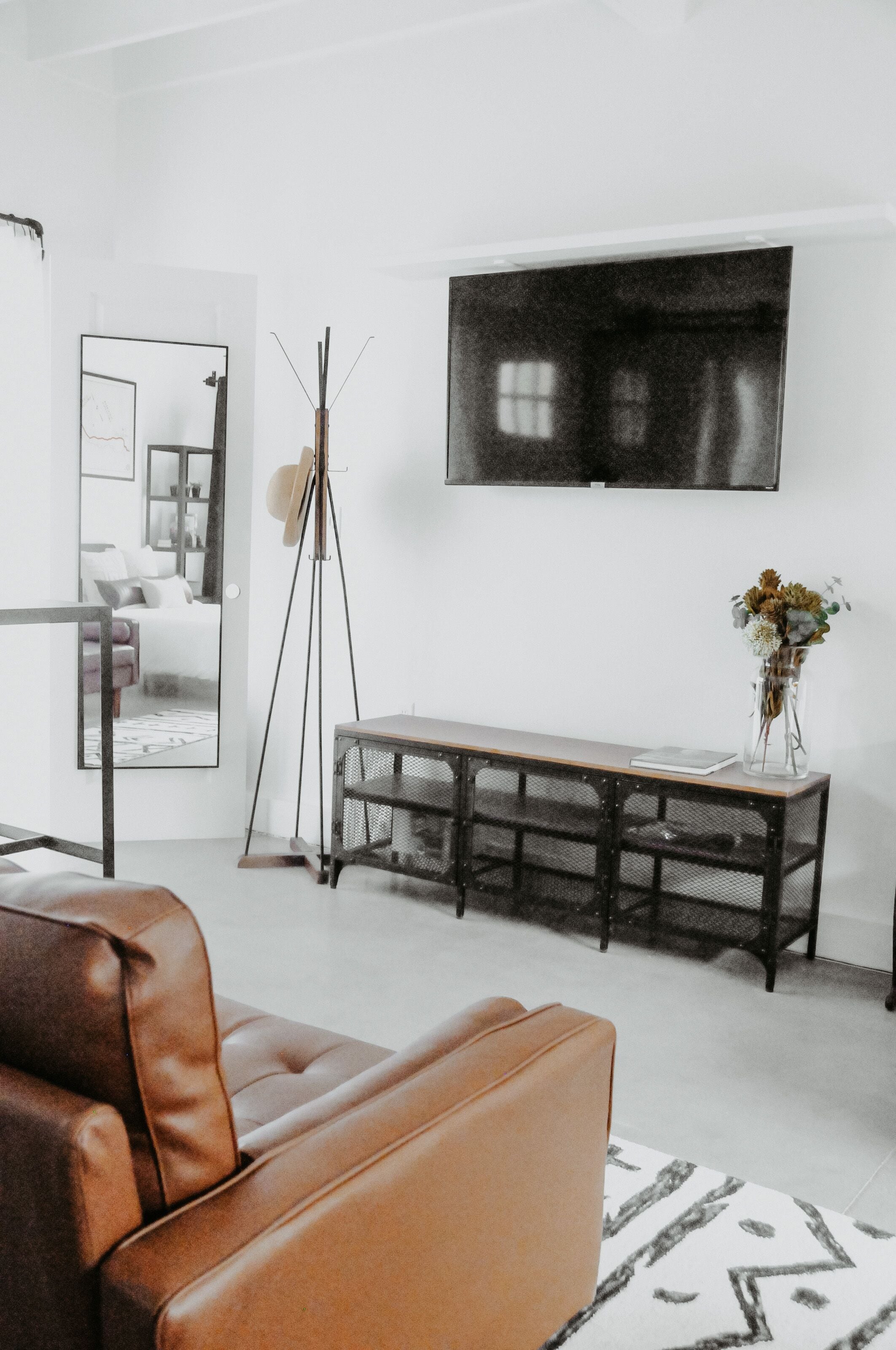 A modern living room with a leather sofa, a wooden coffee table, a large flat-screen TV mounted on the wall, and a mirror reflecting the room.