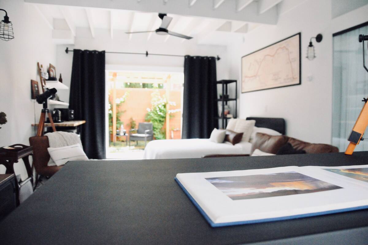 A modern bedroom with a bed, a desk with a laptop, and a view of the outdoors.