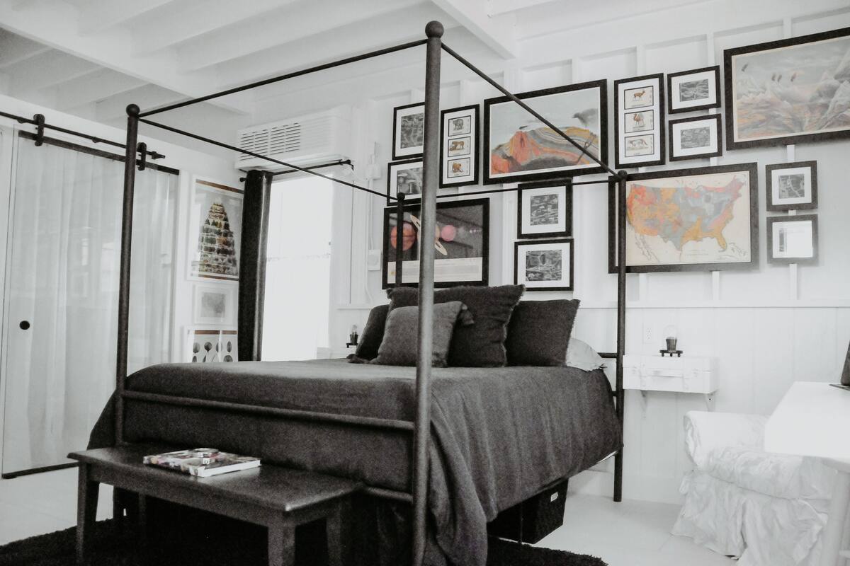 A modern bedroom with a four-poster bed, a bedside table, and a wall decorated with framed artwork.