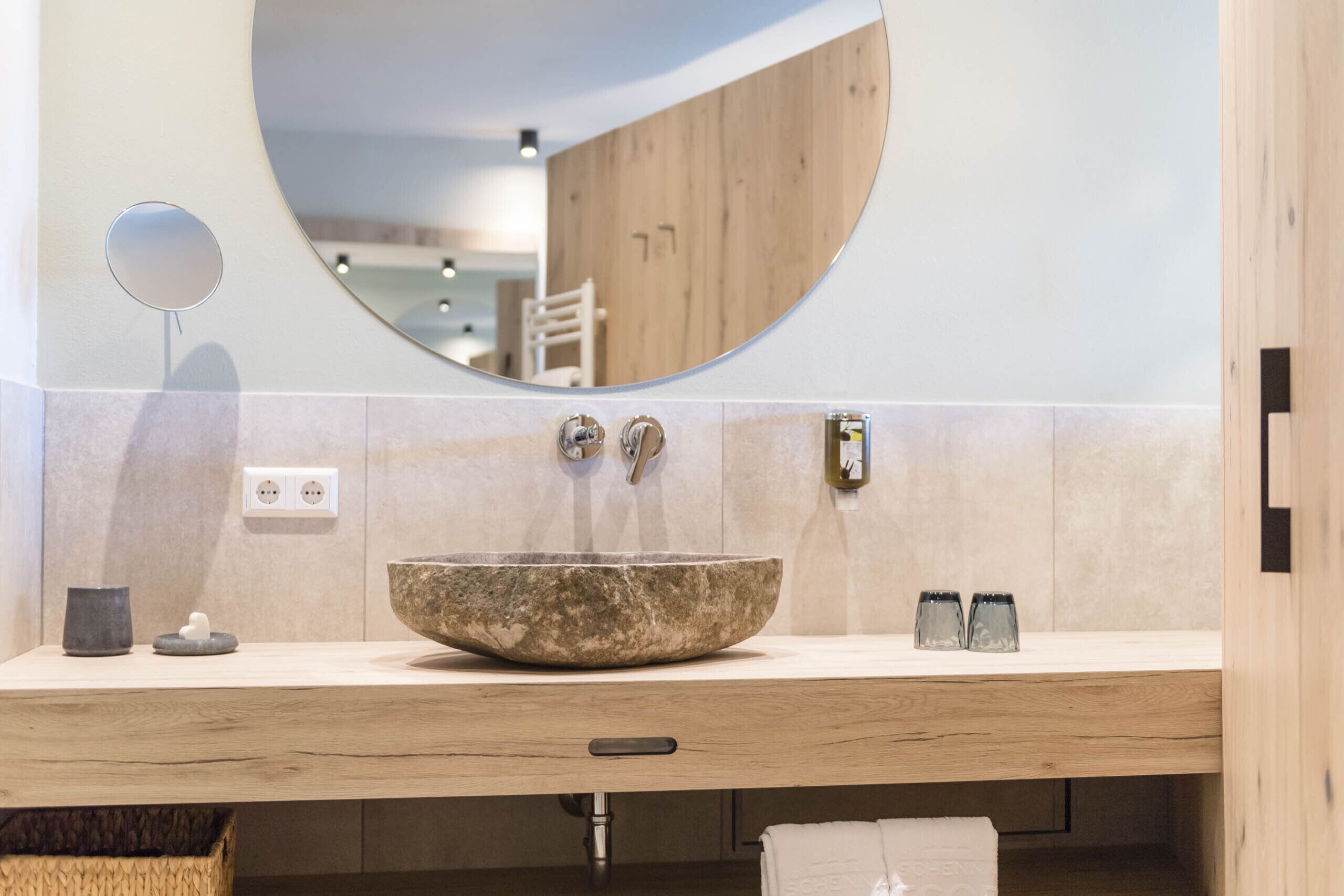 A modern bathroom with a round mirror, a stone basin, and wooden accents.