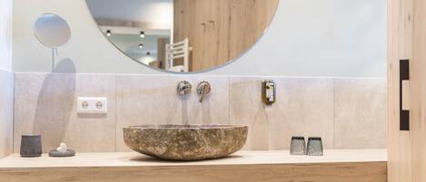 A modern bathroom with a round mirror, a stone basin, and wooden accents.