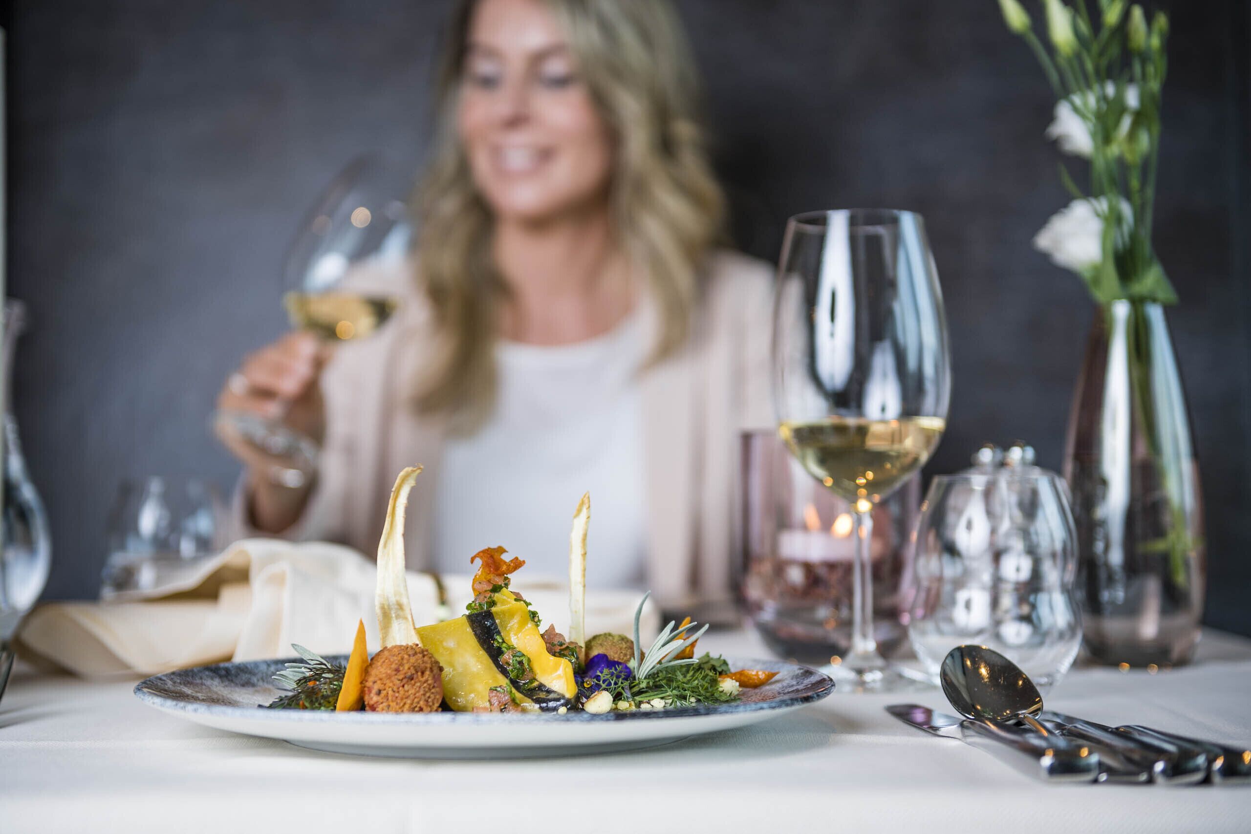 Een eettafel met een bord eten, een glas witte wijn en een vaas vol bloemen.