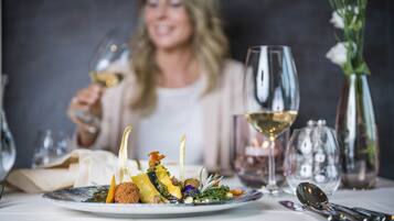 Een eettafel met een bord eten, een glas witte wijn en een vaas vol bloemen.