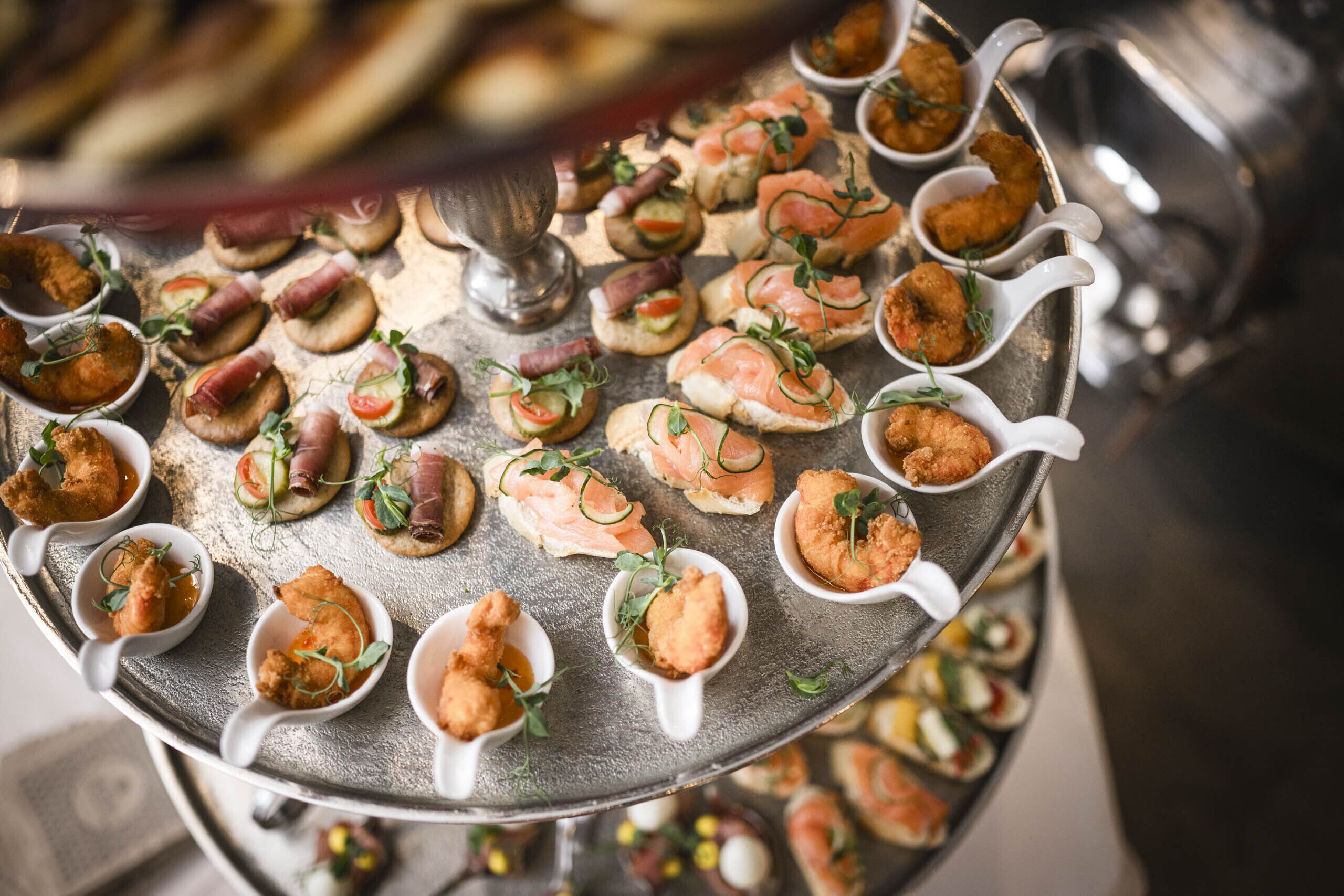 A variety of appetizers arranged on a metal tray, including items like smoked salmon, prosciutto, and possibly some seafood or vegetable-based dishes.