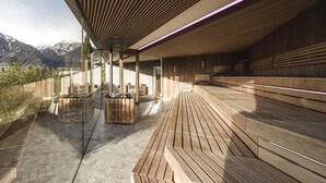 Zona relax esterna moderna con panche in legno e struttura in vetro, affacciata su un paesaggio montuoso.