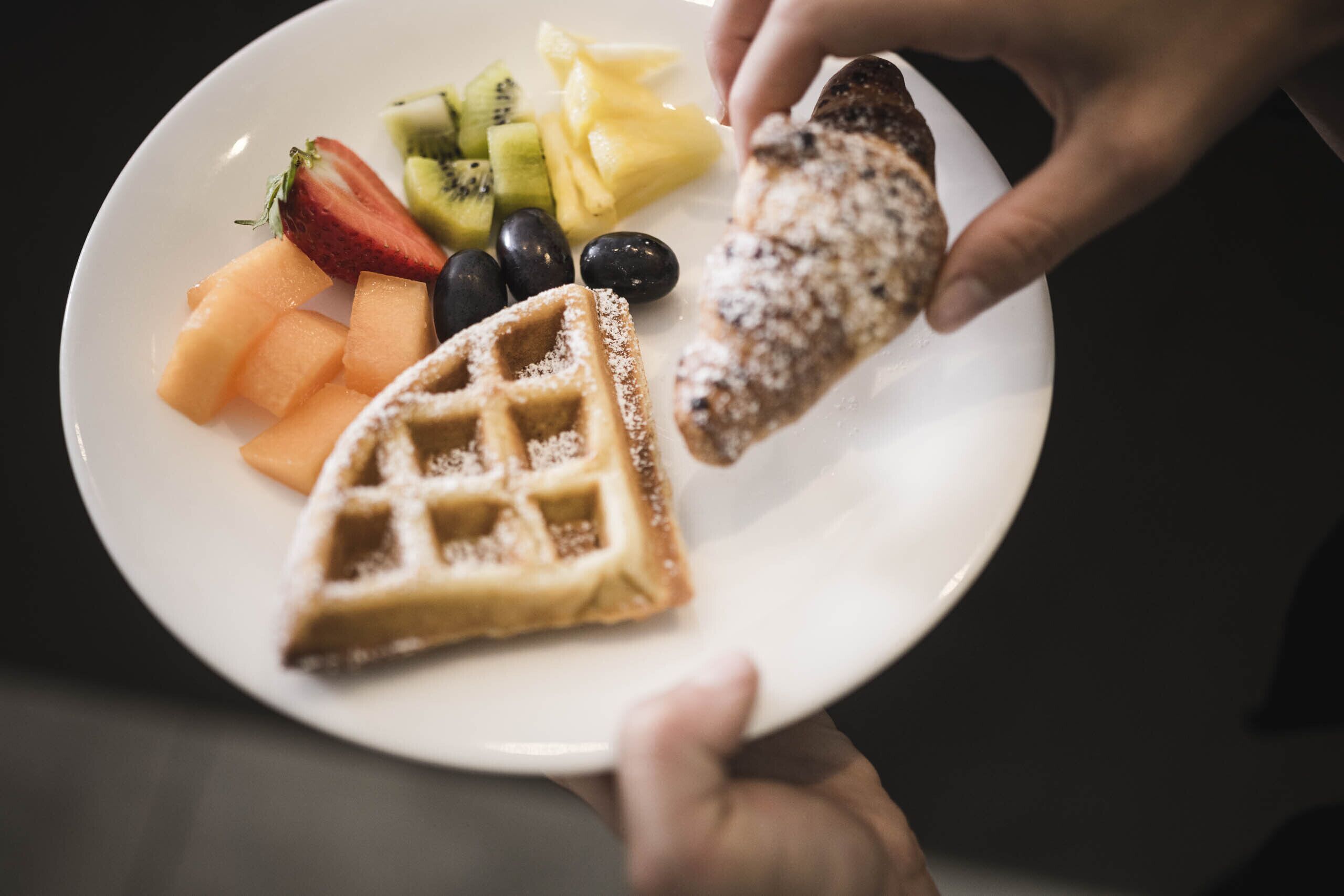 Une assiette avec une gaufre, des fraises, des kiwis, de l’ananas et des myrtilles.