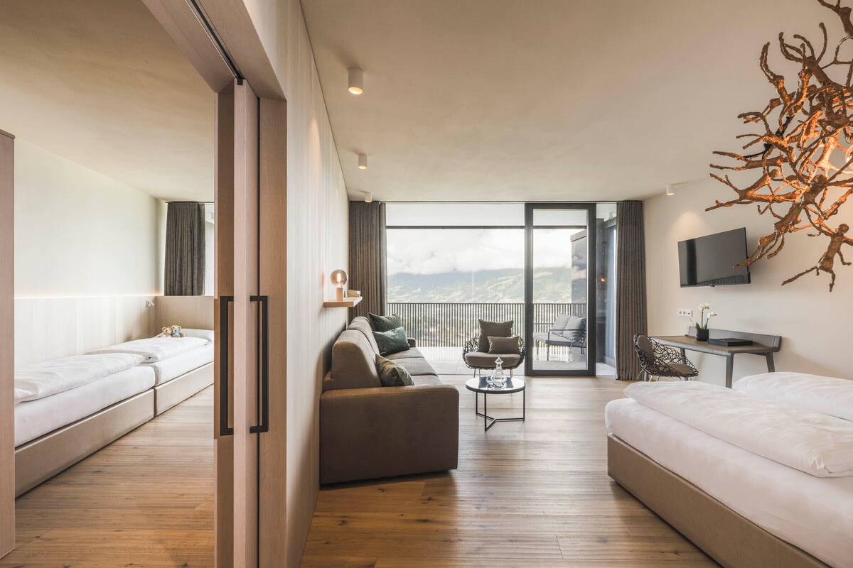 A modern hotel room with a balcony, a sofa, a small table, and a TV.