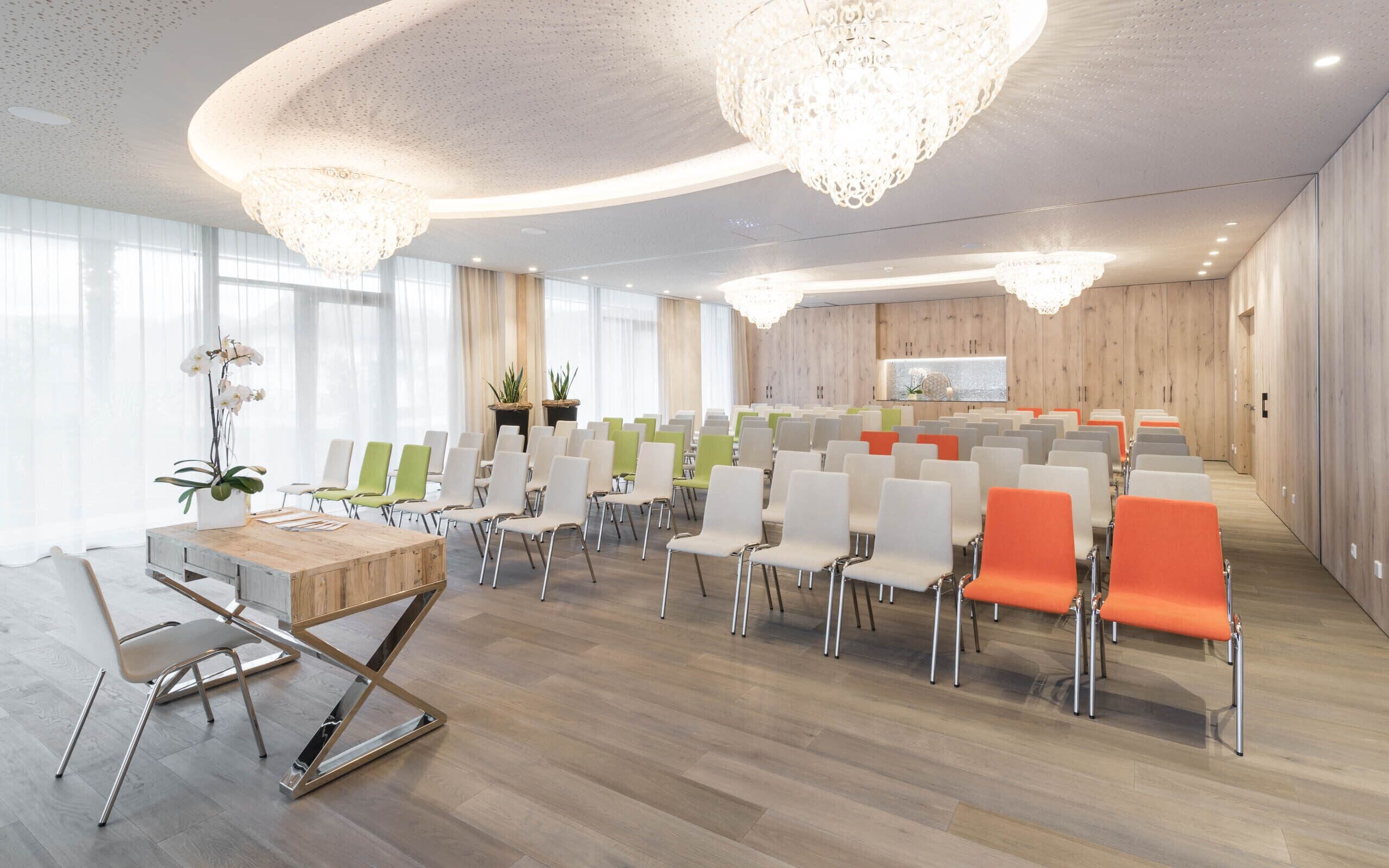 A conference room with rows of chairs, a wooden table, and a large window.