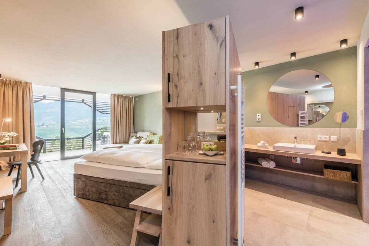 A modern hotel room with a large bed, a desk, and a balcony with a view.