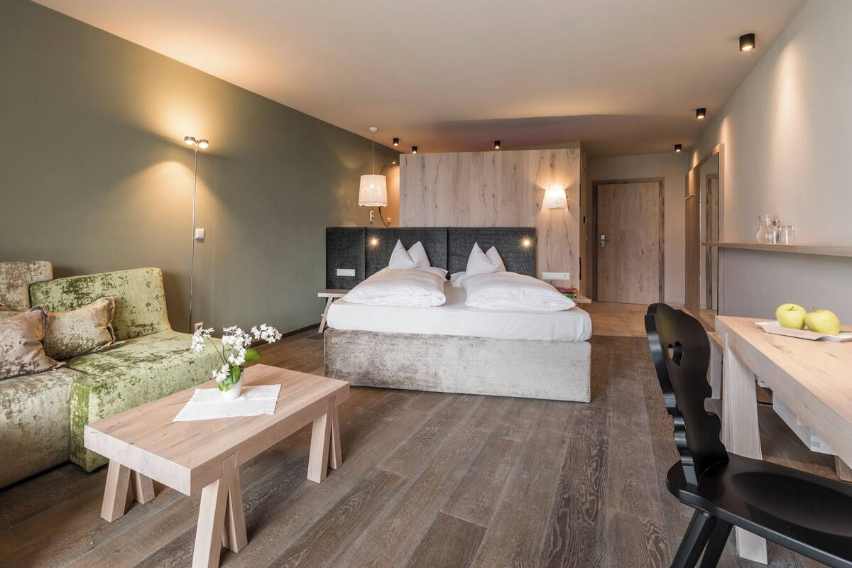 A modern hotel room with a bed, a sofa, a desk, and a chair.