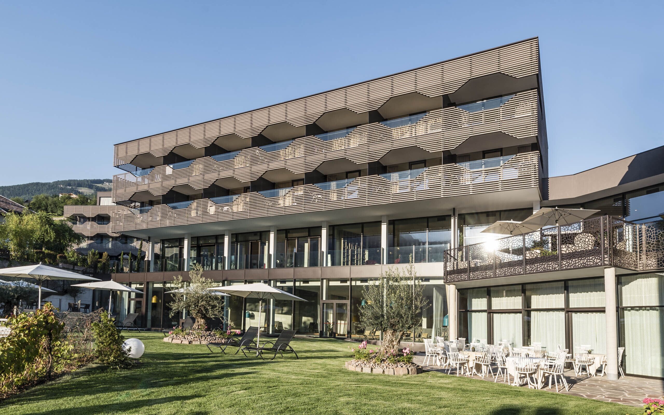 Un edificio moderno con una fachada geométrica singular, zona de estar al aire libre y un césped bien cuidado.