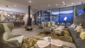 Un'area lounge moderna con camino, posti a sedere confortevoli, un bar e ampie finestre con vista sulle montagne.