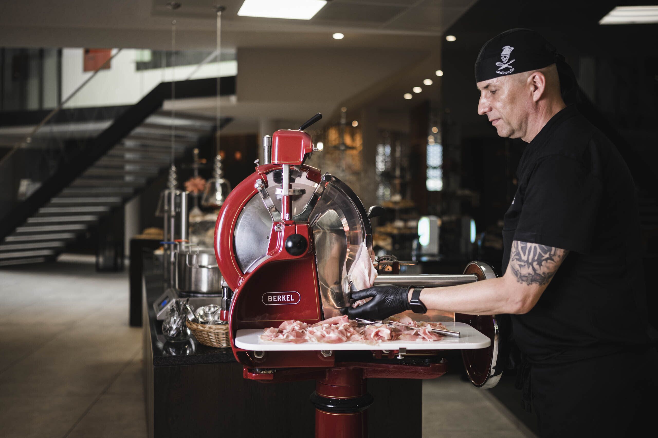 Una persona usando un cortador de carne rojo Berkel en una cocina moderna.
