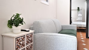 Un salon moderne avec un canapé gris, un meuble blanc orné de motifs décoratifs, une plante en pot et des œuvres d’art accrochées au mur.