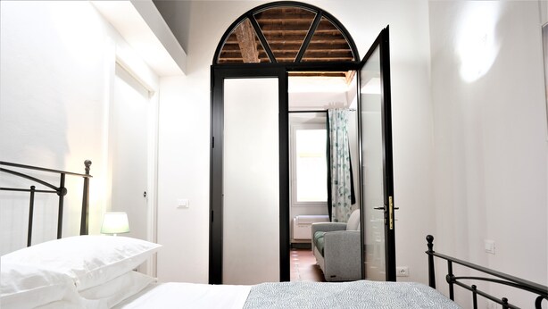 Une chambre à coucher comprenant un lit, une chaise, une lampe et une porte donnant sur une autre pièce.