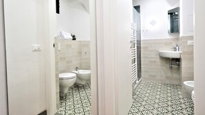 Une salle de bain avec un sol carrelé de blanc, un lavabo blanc, un bidet et une douche.
