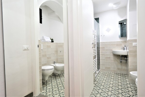 A bathroom with a white tiled floor, a white sink, a bidet, and a shower.