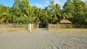 A sandy beach with a wooden fence, palm trees, and a thatched-roof hut. - Sablayan Paraiso Beach Resort (Sablayan)