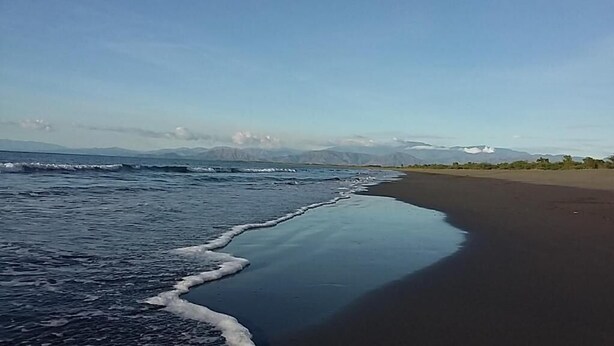 A beach with waves lapping onto the shore, a clear sky, and distant mountains. - Sablayan Paraiso Beach Resort (Sablayan)