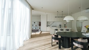 A modern kitchen with a central island, pendant lighting, and a dining area with a dark table and chairs. - Villa Yuna (Canggu)