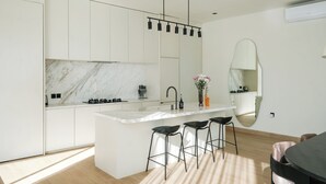 A modern kitchen with white cabinetry, a marble backsplash, and a central island with bar stools. - Villa Yuna (Canggu)
