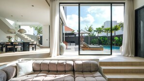 A modern living room with a large sofa, a staircase, and a view of a pool and outdoor area. - Villa Yuna (Canggu)