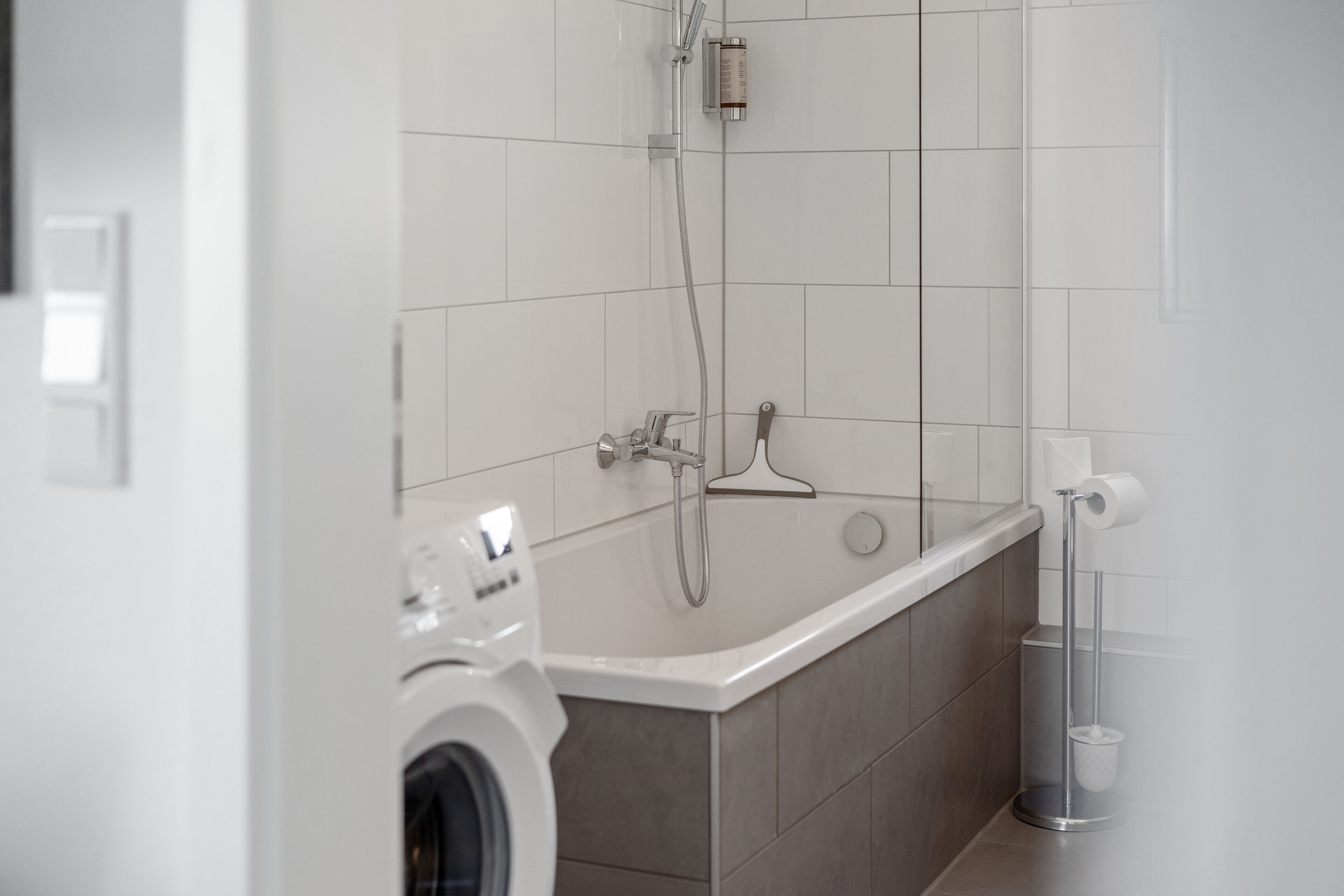 A modern bathroom with a built-in washing machine, a shower, and a toilet paper holder.