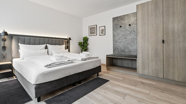 A modern bedroom with a large bed, a wardrobe, a bedside table, and a small plant. - BRIGHT Herzogenaurach Zentrum (Herzogenaurach)