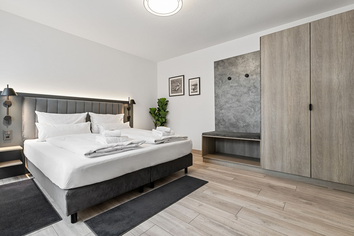 Een moderne slaapkamer met een groot bed, een kledingkast, een nachtkastje en een kleine plant.