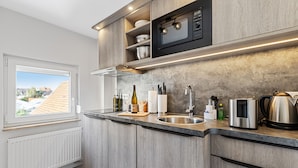 A modern kitchen with a built-in oven, a window with a view, and a countertop with various kitchen items. - BRIGHT Herzogenaurach Zentrum (Herzogenaurach)