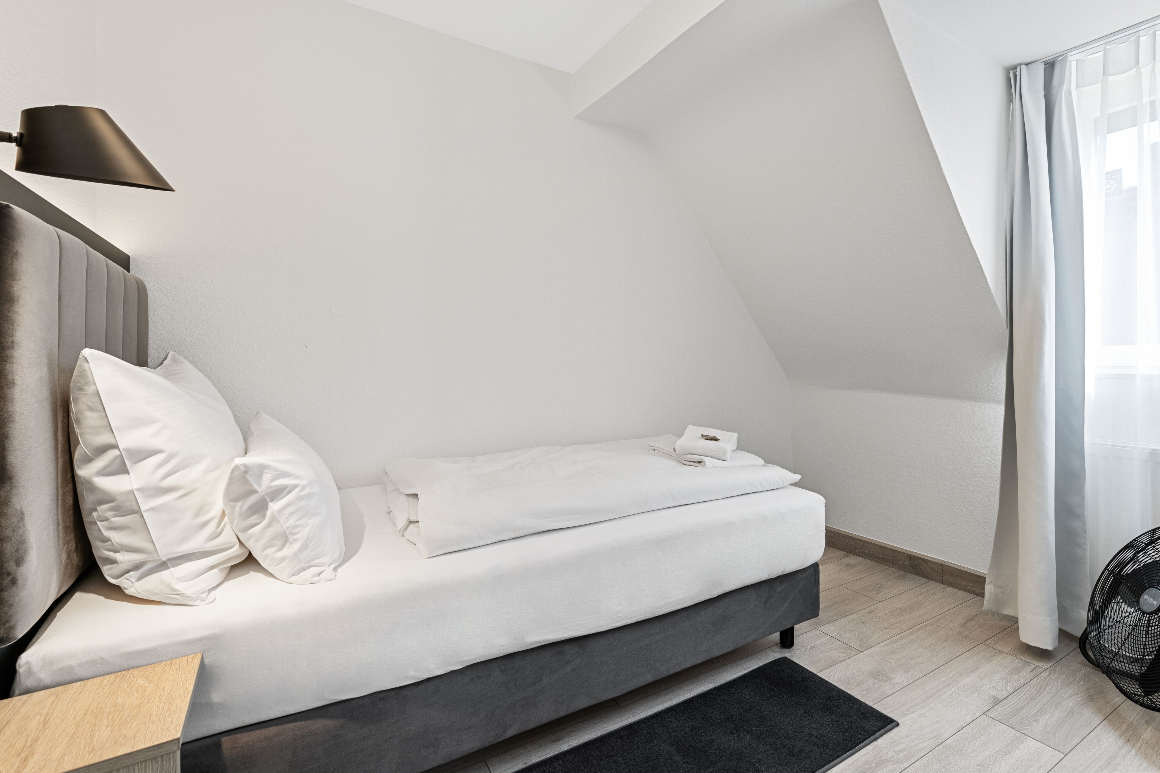 A modern, minimalist bedroom with a bed, pillows, a bedside table, and a lamp.