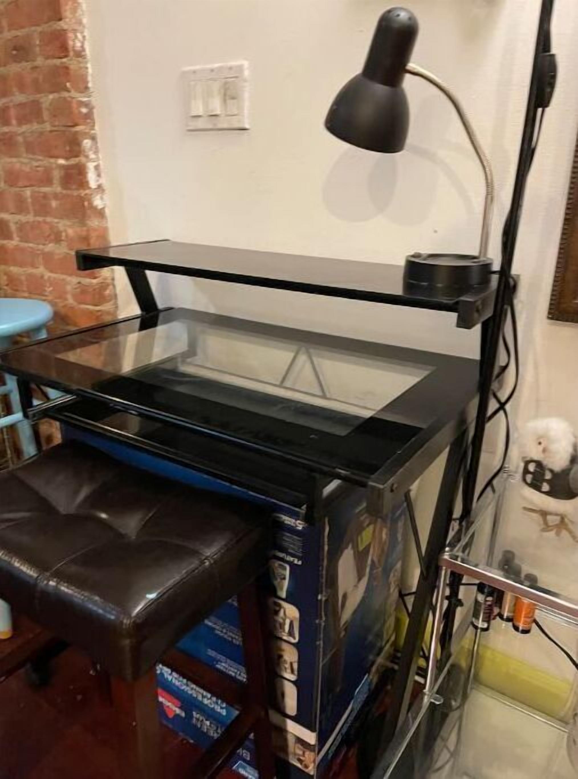 A compact, modern room with a glass-top desk, a black leather chair, and a small blue stool.