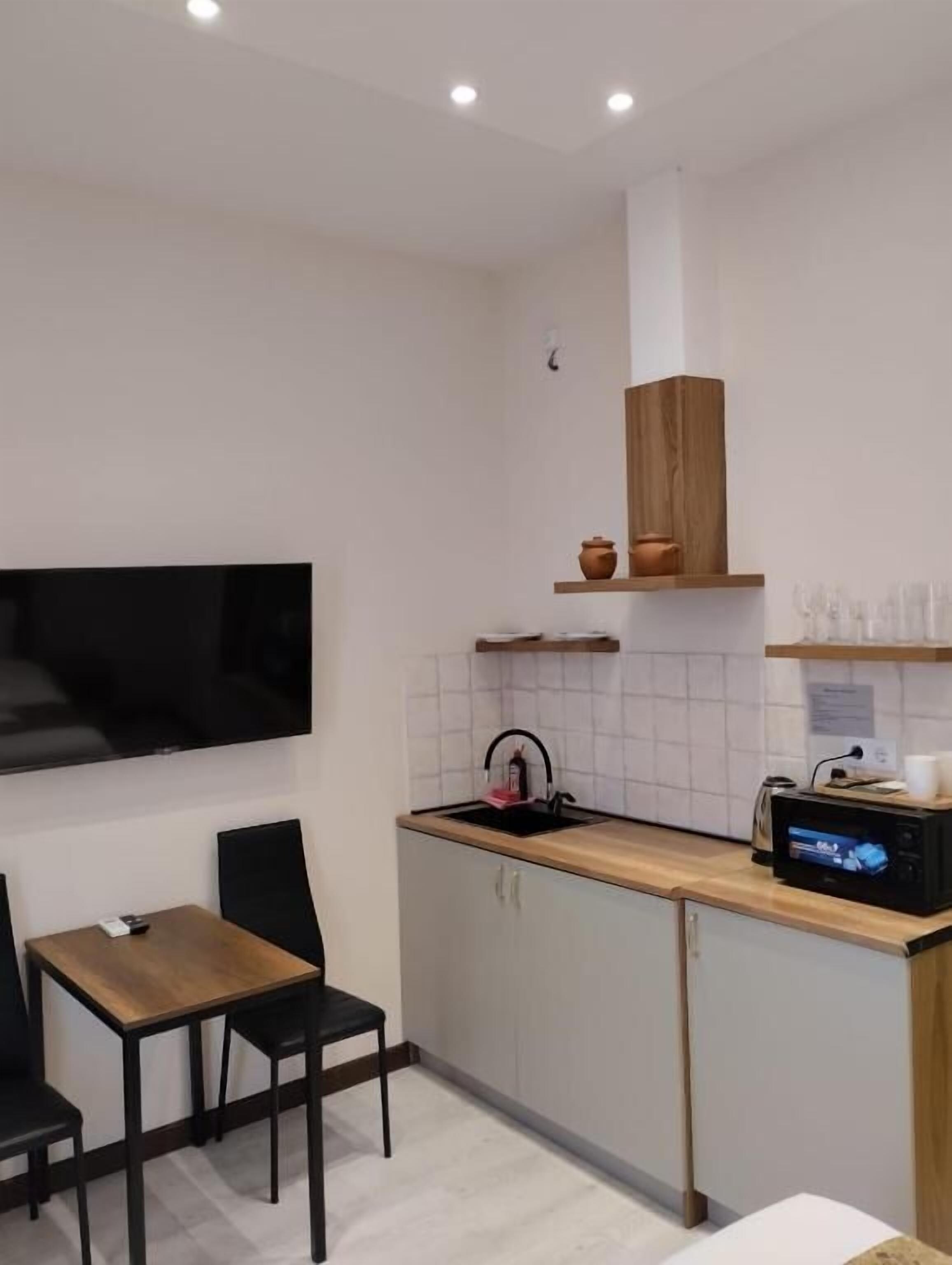 Cocina compacta con encimera de madera, horno empotrado y televisor de pared.