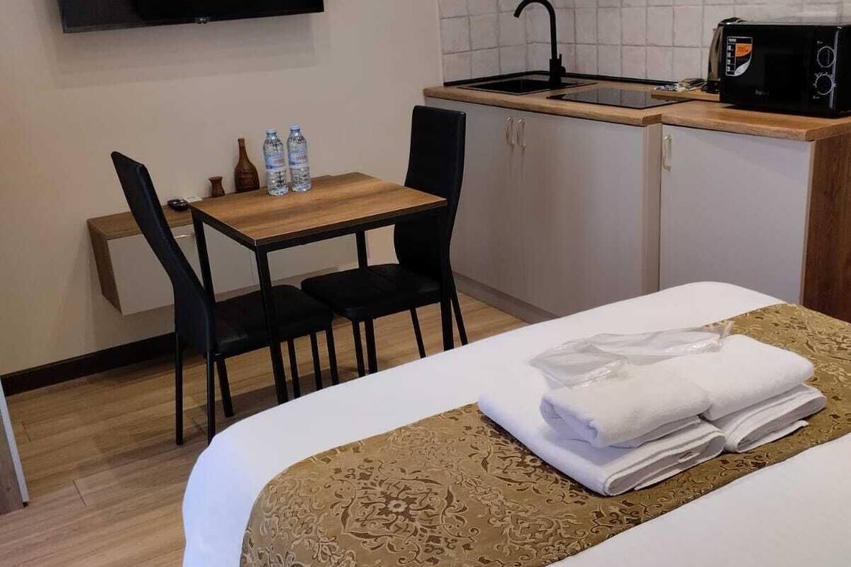 Ett hotellrum med en säng, ett skrivbord med stolar, ett litet kök och en tv med platt skärm.