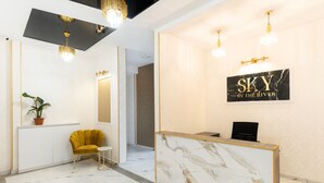 A reception area with a marble reception desk, a yellow chair, and a potted plant. - Sky By The River (Tbilisi)
