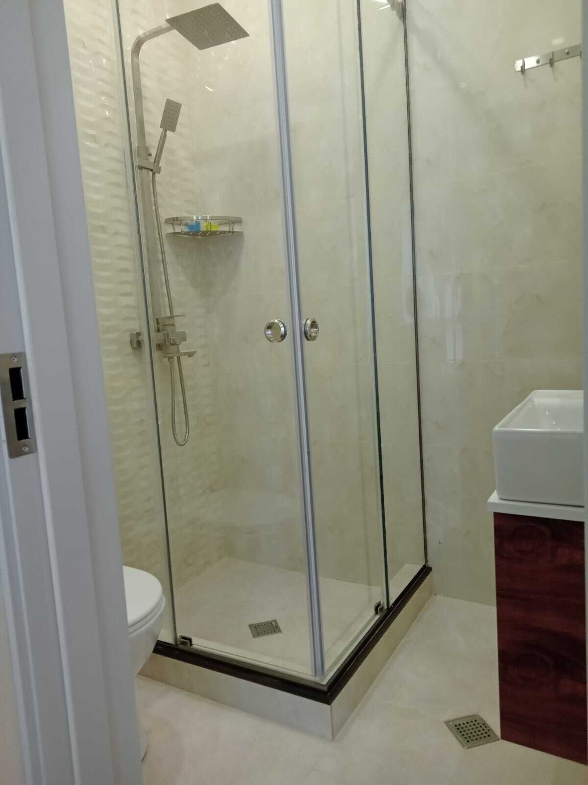Un box de ducha con paredes de cristal, con ducha de mano y grifo empotrado.