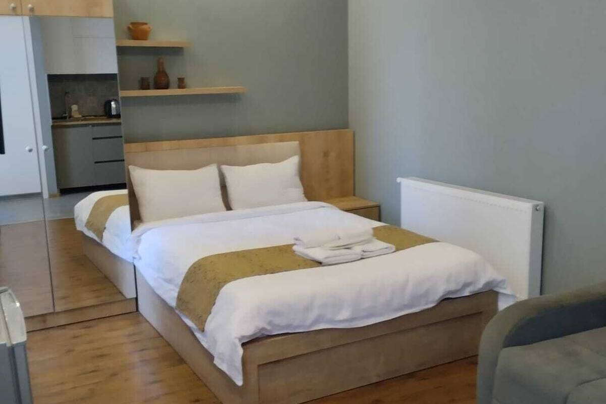 Ett modernt sovrum med en säng i trä, ett sängbord och en inbyggd hylla med dekorativa föremål.