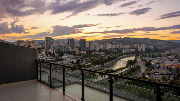 A cityscape with a river, buildings, and a clear sky. - Sky By The River (Tbilisi)