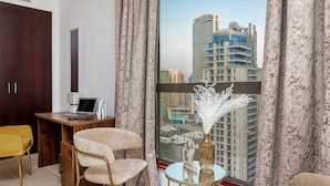 A modern room with a desk, a laptop, a chair, and a view of a cityscape through large windows. - 2BR apartment 2 minutes to beach Amwaj 4 (Dubai)