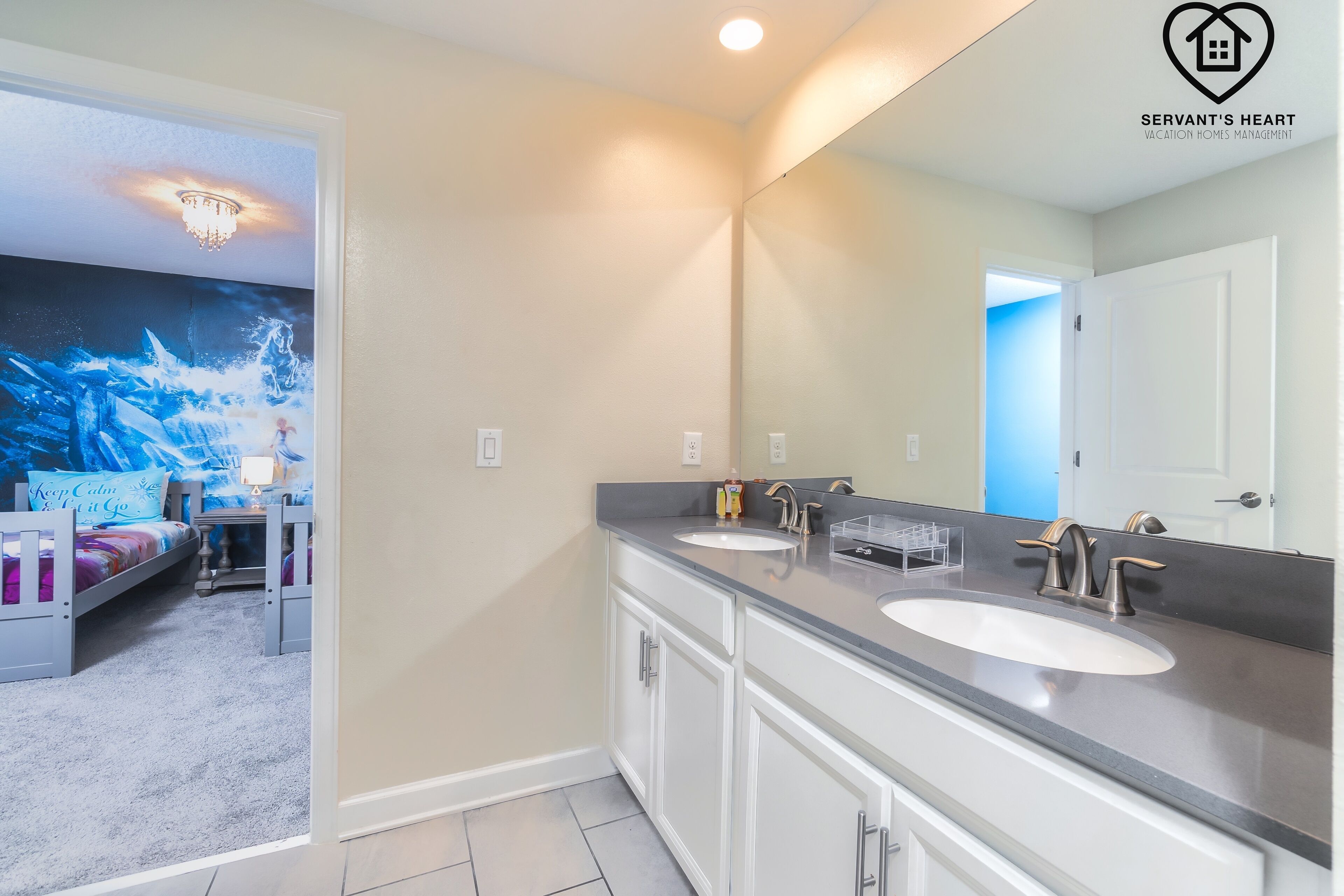 A bathroom with two sinks, a large mirror, and a door leading to another room.