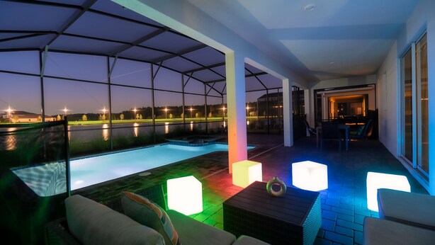 Ein überdachter Außenbereich mit Swimmingpool, Sitzgelegenheiten und Blick auf einen See im Abenddämmerung.