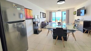 A modern kitchen with a refrigerator, a dining table with chairs, and a view of the beach through large windows. - Oceanfront white sand beach condo  (Cancun)