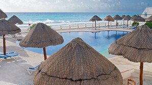 A poolside area with thatched umbrellas, lounge chairs, and a view of the ocean. - Oceanfront white sand beach condo  (Cancun)