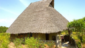 A thatched-roof hut with a stone wall, surrounded by vegetation. - Masai Mara Explore Camp (Narok)